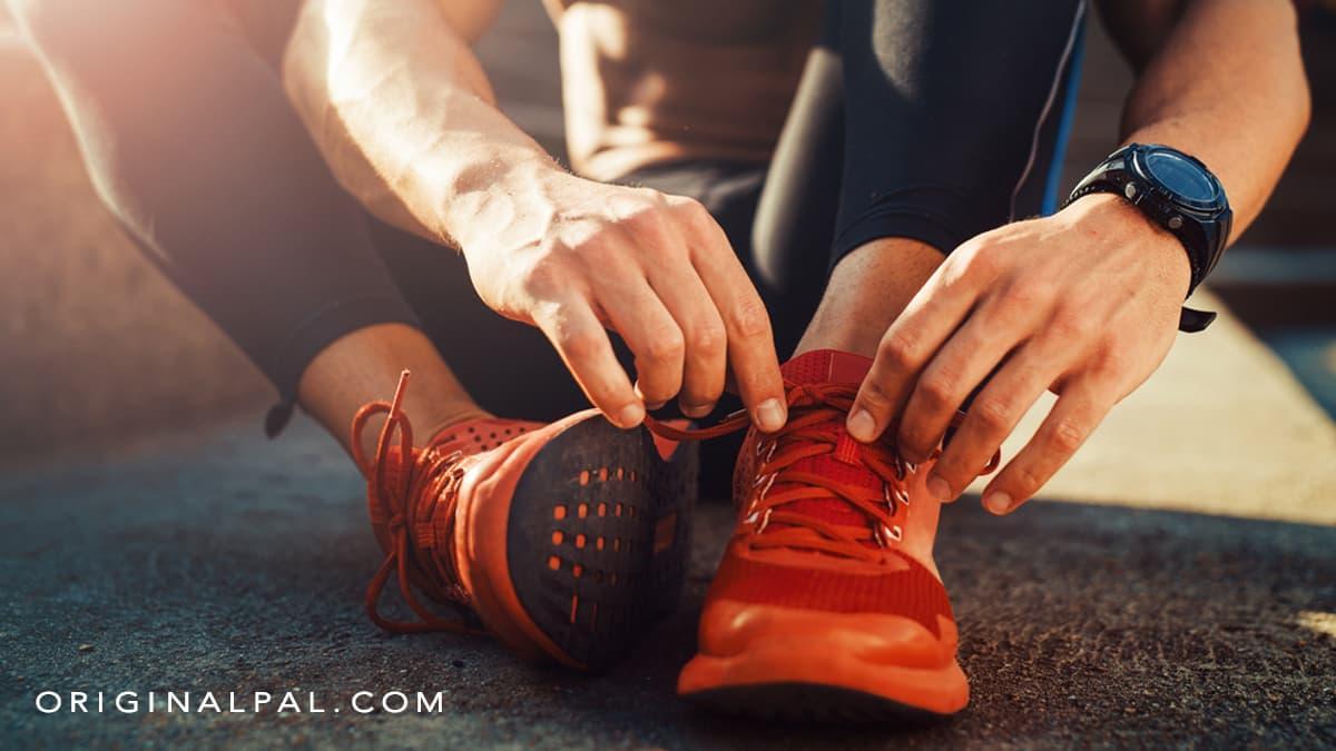 کفش ورزشی نارنجی رنگ در پای ورزشکار نشسته بر زمین ورزشی